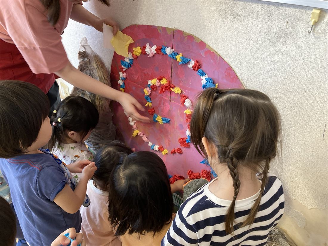 紙を丸めた色とりどりの花を、子どもたちが大きな赤い台紙に貼っている