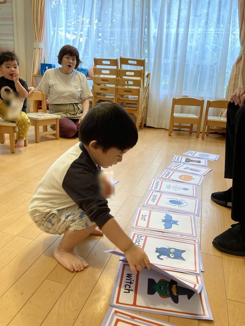 床に並んだ英語のカードを、子どもがしゃがんで選んでいる